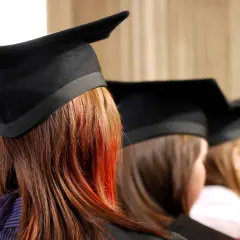 Graduates in caps, one with striking red streaks in her hair, await their business essentials certificate.