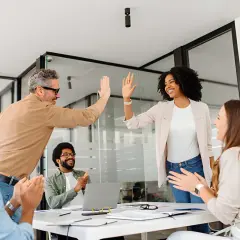 Team celebrates success after a leadership communication training session. High-fives and smiles abound as they master new skills.