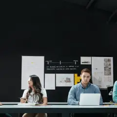 Four diverse individuals engage in a front line manager training session, collaborating around a table with laptops and notebooks.