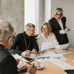 A diverse team collaborates on charts and documents, showcasing effective leadership in a hybrid work environment.