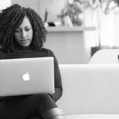 A woman with curly hair focuses on her laptop, engaged in virtual leadership development.