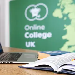 A laptop and open books on a desk, with a green banner in the background displaying "Online College UK" and a map of Great Britain.