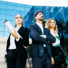 Three professionals stand confidently before a modern building, ready to embrace the future with a certificate in information technology online.