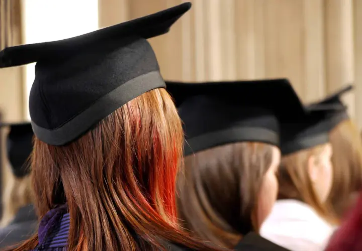 Graduates in caps, one with striking red streaks in her hair, await their business essentials certificate.