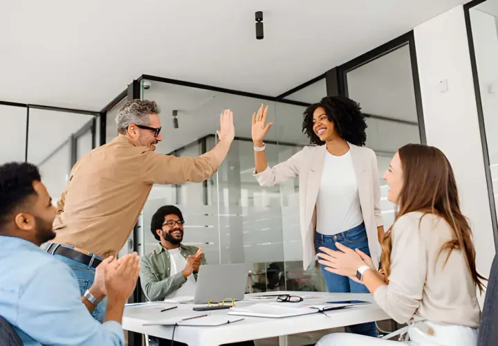Team celebrates success after a leadership communication training session. High-fives and smiles abound as they master new skills.