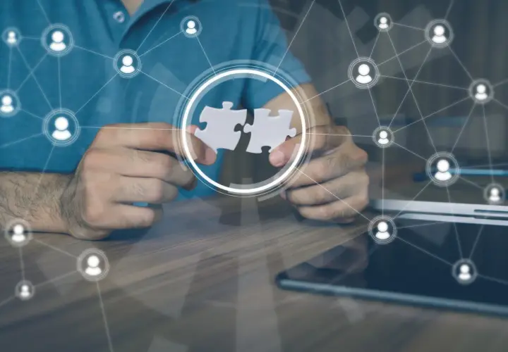 Hands connect puzzle pieces, symbolizing collaboration and leading a remote team through a network of connected people icons.