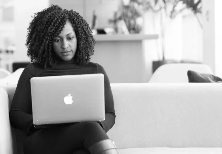 A woman with curly hair focuses on her laptop, engaged in virtual leadership development.