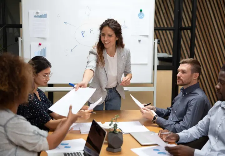 A woman leads a delegation training session, handing out papers to her team during a meeting.