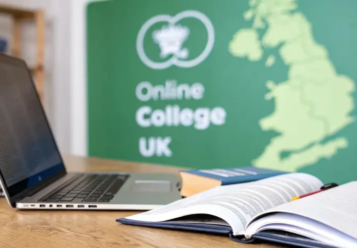 A laptop and open books on a desk, with a green banner in the background displaying "Online College UK" and a map of Great Britain.