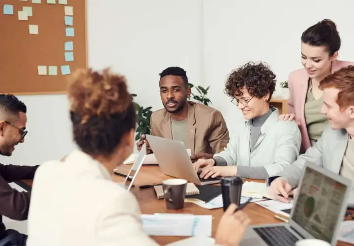 A diverse team collaborates, showcasing high employee engagement and motivation as they brainstorm ideas around a table with laptops and notes.