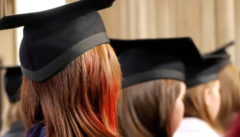 Graduates in caps, one with striking red streaks in her hair, await their business essentials certificate.