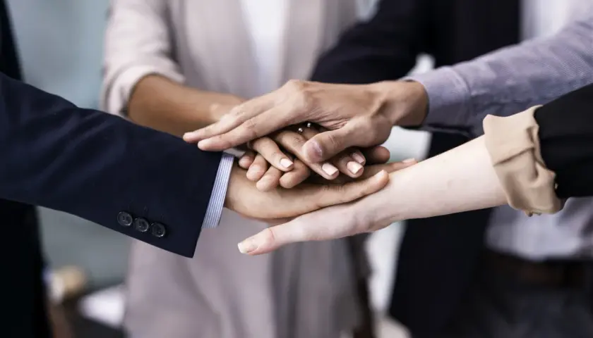 A diverse group of people stack their hands, symbolizing unity and teamwork. This image shows why is respect important for building strong connections.