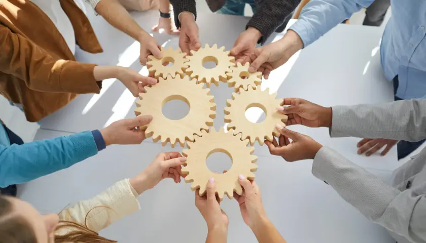 Hands connect wooden gears, symbolizing teamwork and collaboration training. Each piece fits perfectly, showing how individuals work together.