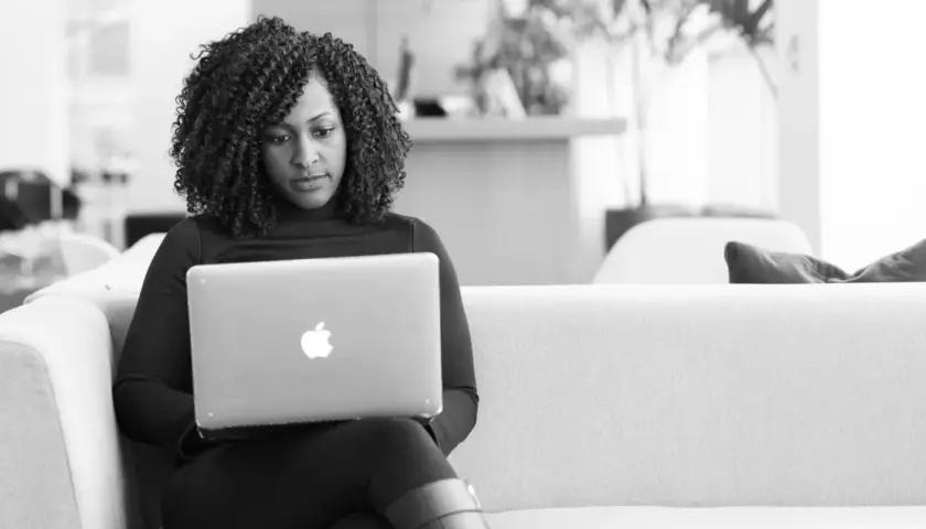 A woman with curly hair focuses on her laptop, engaged in virtual leadership development.