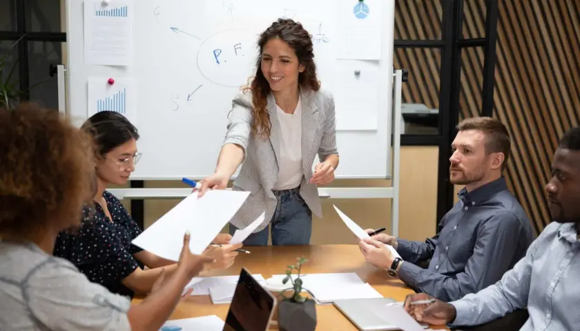 A woman leads a delegation training session, handing out papers to her team during a meeting.