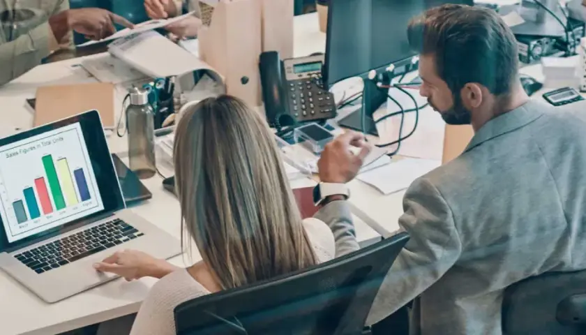 Colleagues analyze sales data on a laptop, a scene that could be part of an online business intelligence degree program.