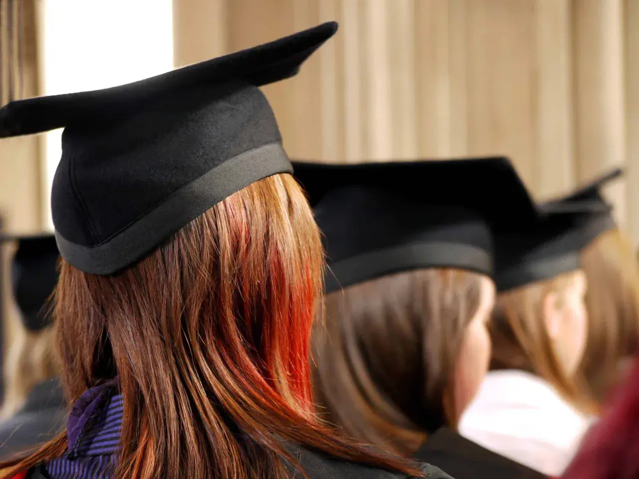 Graduates in caps, one with striking red streaks in her hair, await their business essentials certificate.