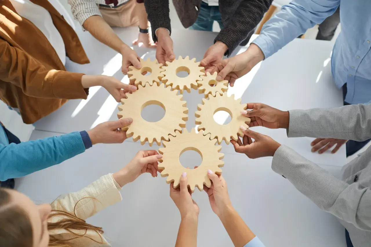 Hands connect wooden gears, symbolizing teamwork and collaboration training. Each piece fits perfectly, showing how individuals work together.