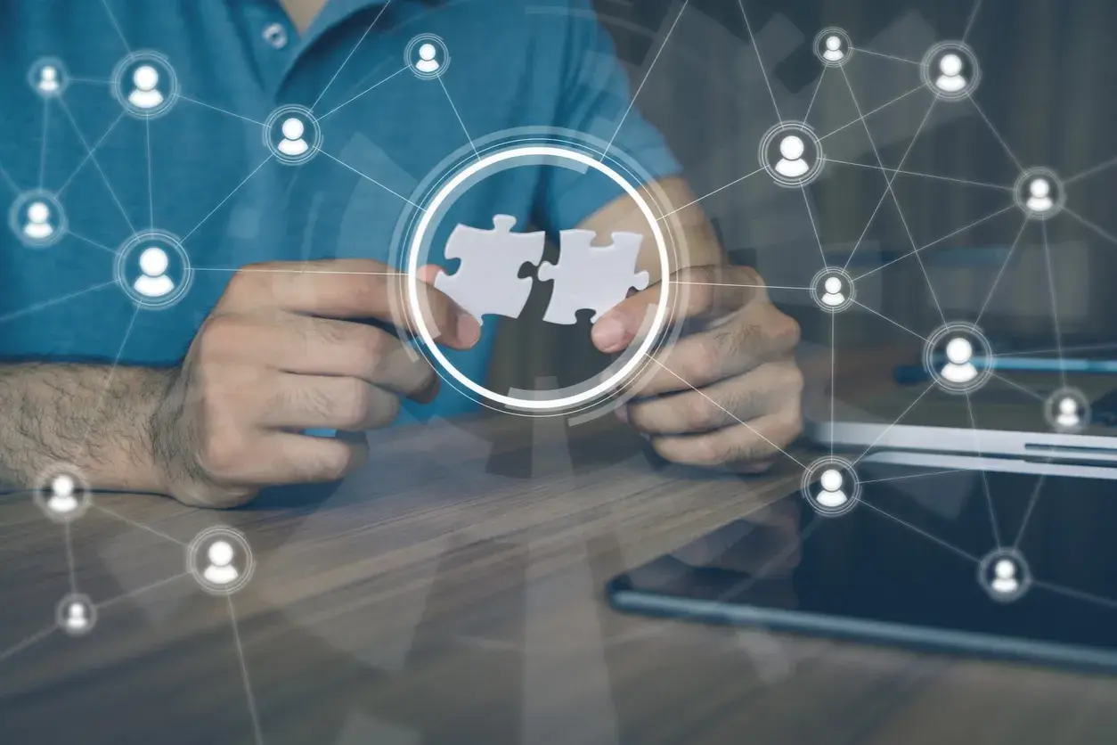 Hands connect puzzle pieces, symbolizing collaboration and leading a remote team through a network of connected people icons.