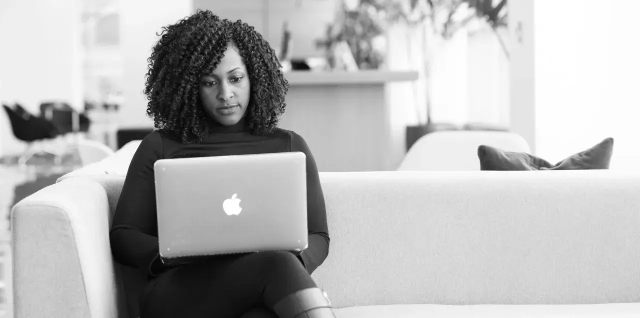 A woman with curly hair focuses on her laptop, engaged in virtual leadership development.