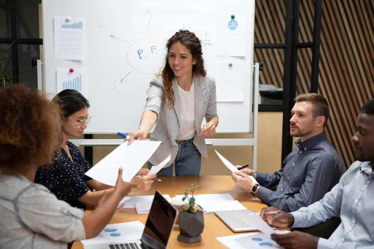 A woman leads a delegation training session, handing out papers to her team during a meeting.