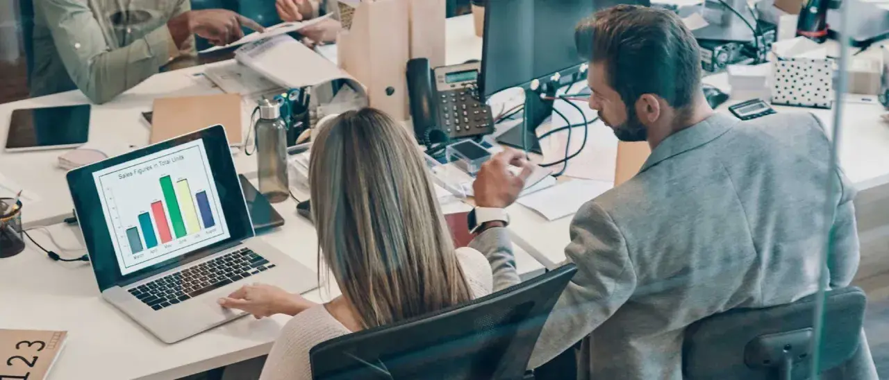 Colleagues analyze sales data on a laptop, a scene that could be part of an online business intelligence degree program.
