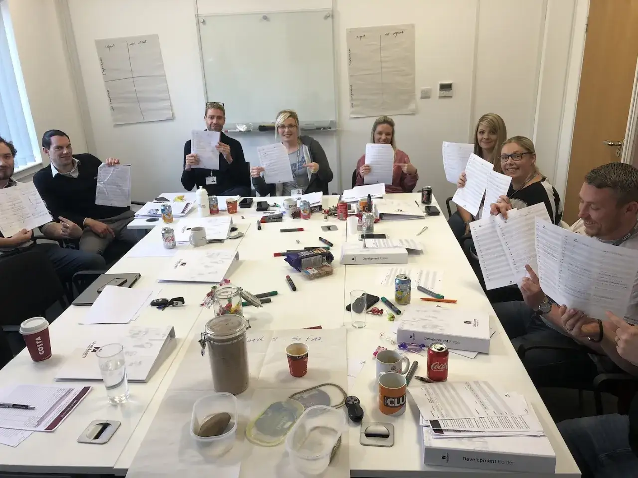 Participants in a leadership development training session review materials. They hold up papers, smiling and engaged.