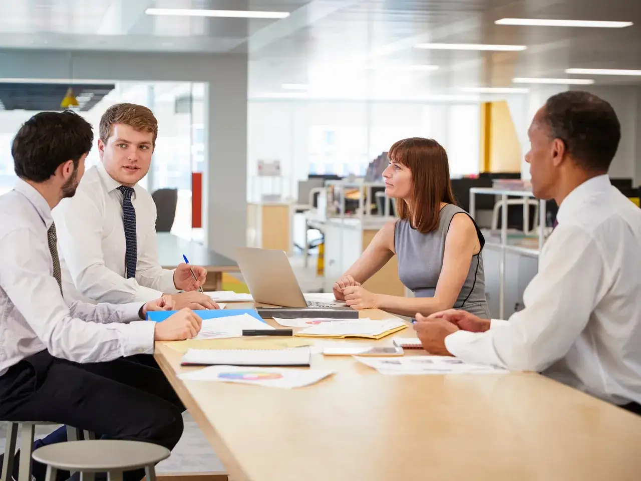 Four colleagues discuss a project, their faces showing a hint of change fatigue as they pore over documents and a laptop.
