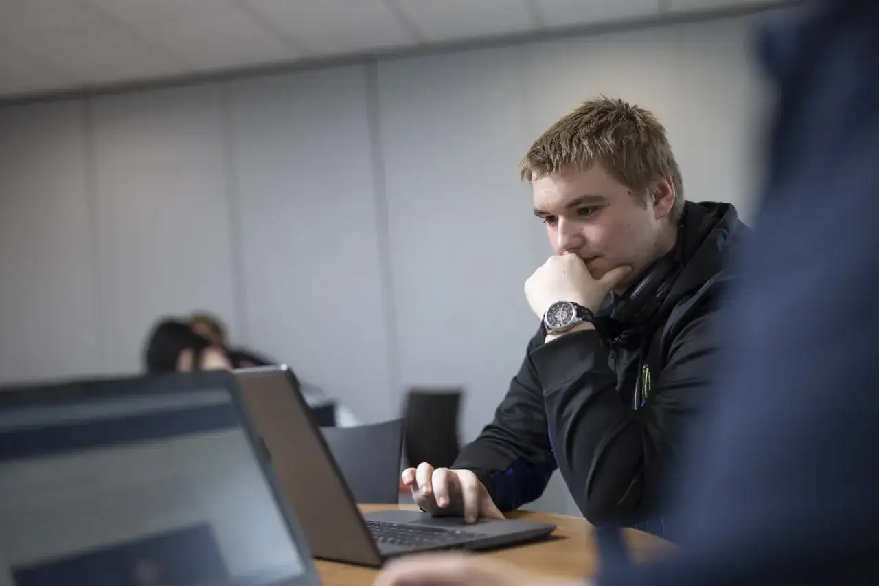 A young man ponders his laptop, a scene embodying what is lifelong education: continuous learning and growth.