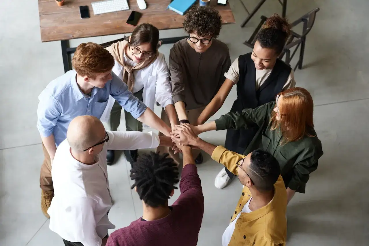 A diverse team joins hands in a circle, symbolizing the keys of communication and shared purpose.
