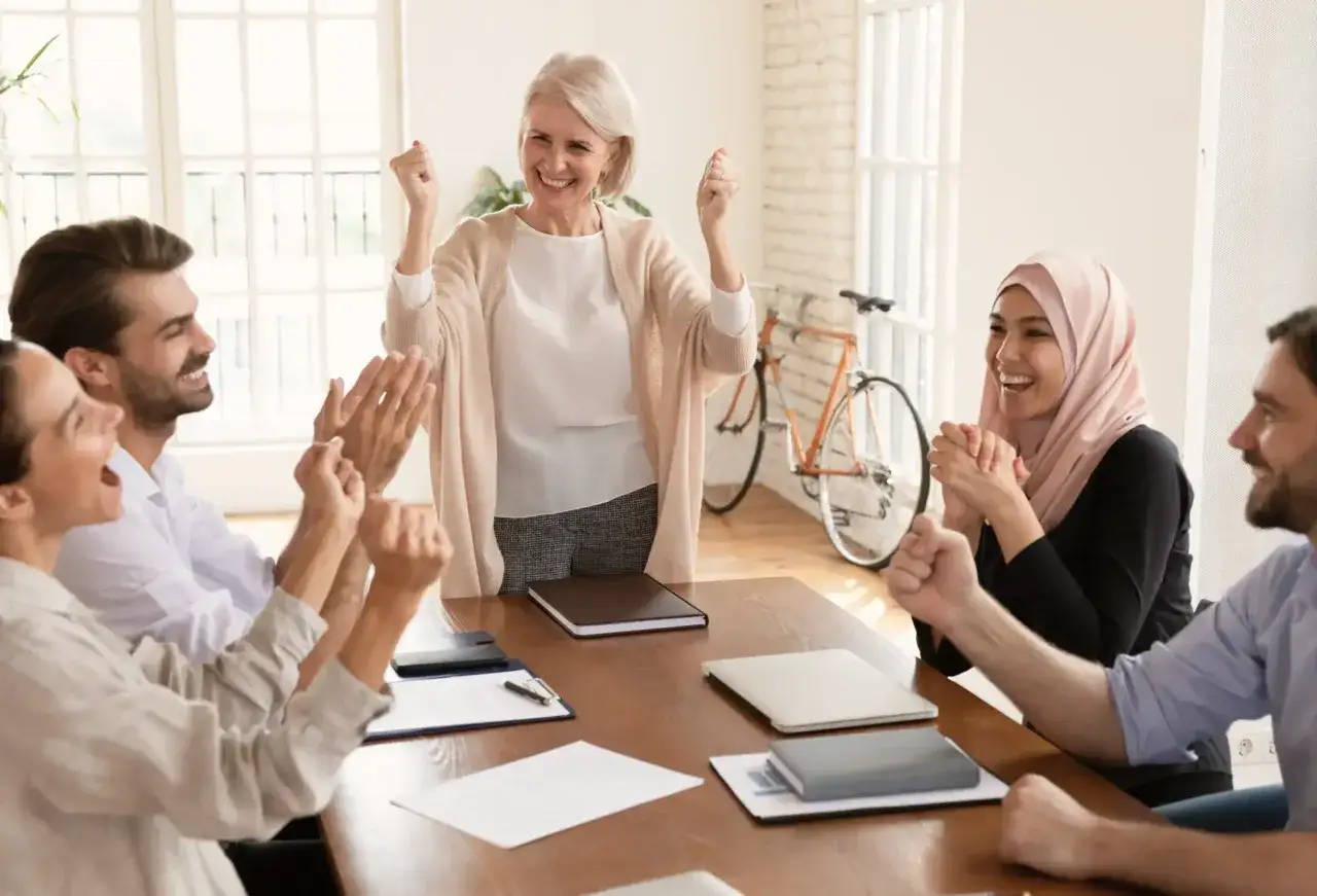 A diverse team celebrates success, showing high employee engagement and motivation. Their joyful expressions and raised fists convey a shared sense of accomplishment.