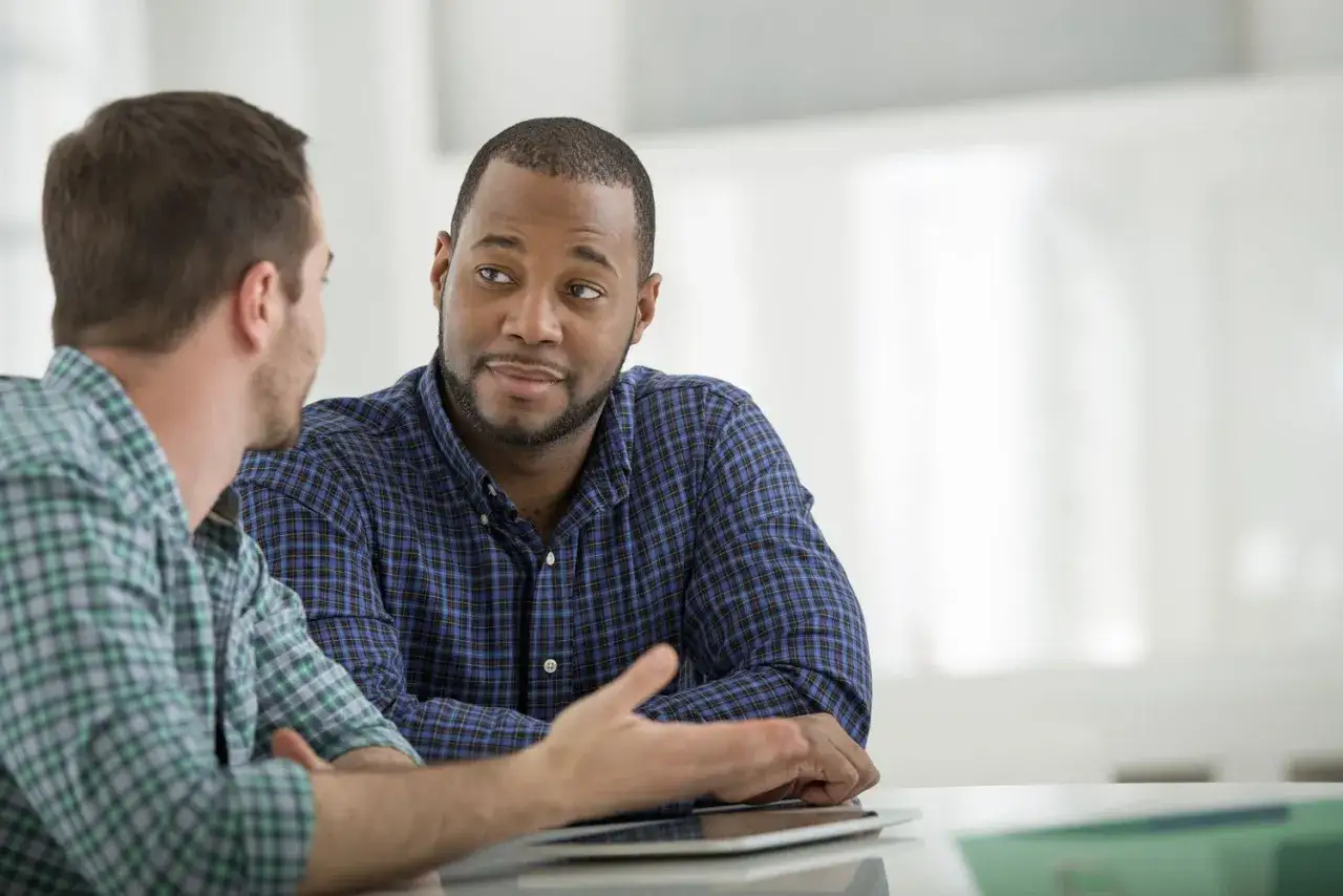 Two men in plaid shirts engage in a serious discussion, demonstrating skills in leading difficult conversations.