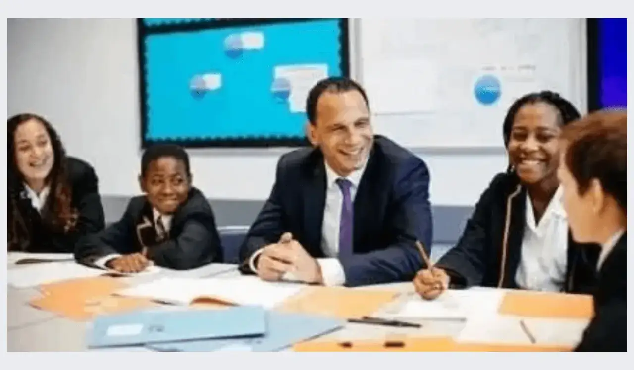 A smiling teacher leads a school leadership training session with diverse students, fostering collaboration and engagement.