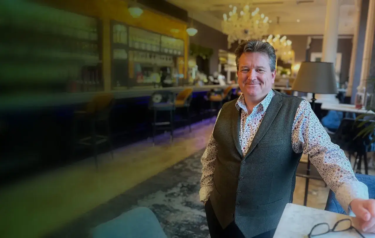 A smiling man in a vest and patterned shirt, embodying leadership resilience training, stands in a stylish bar.