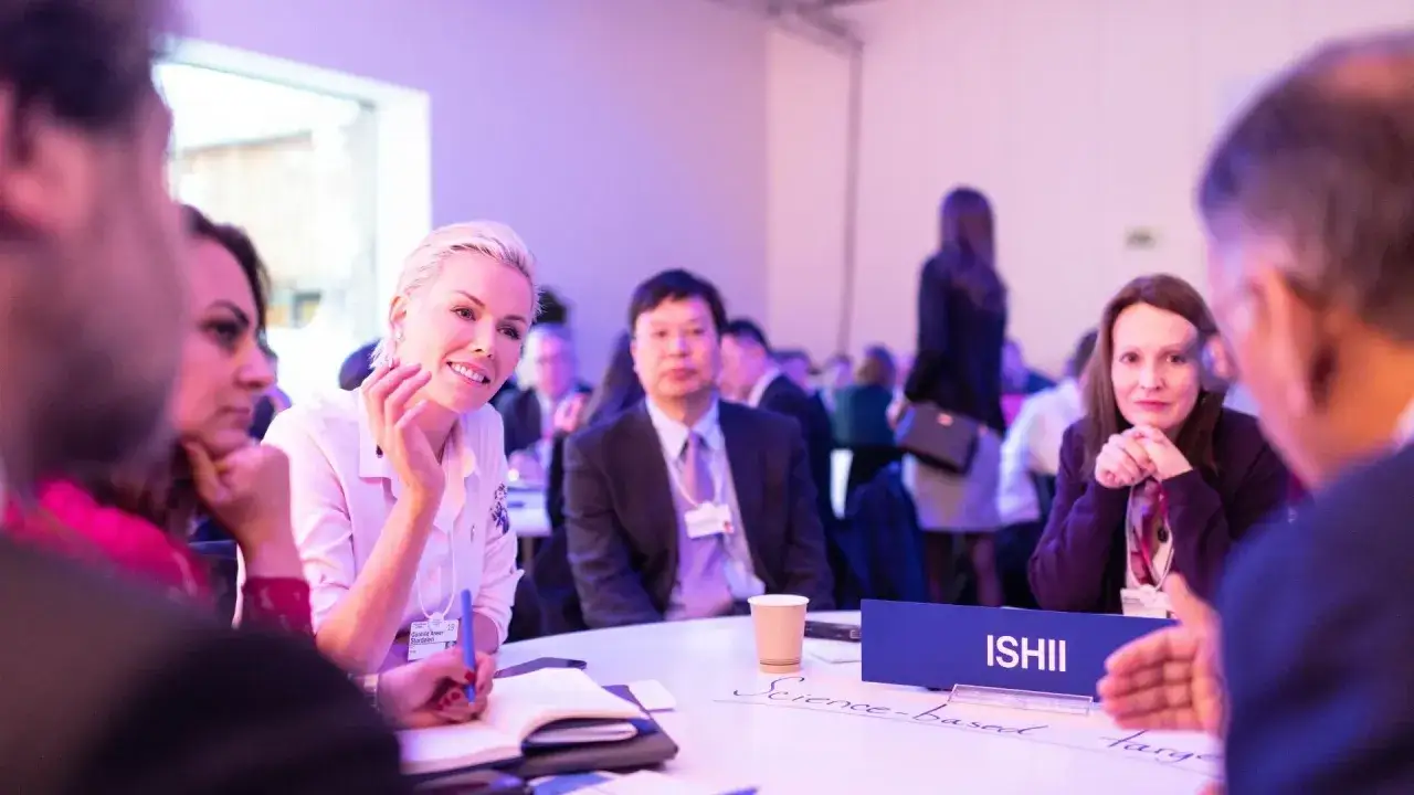 Attendees engage at an internal communications conference, with a woman in a pink shirt smiling and taking notes.
