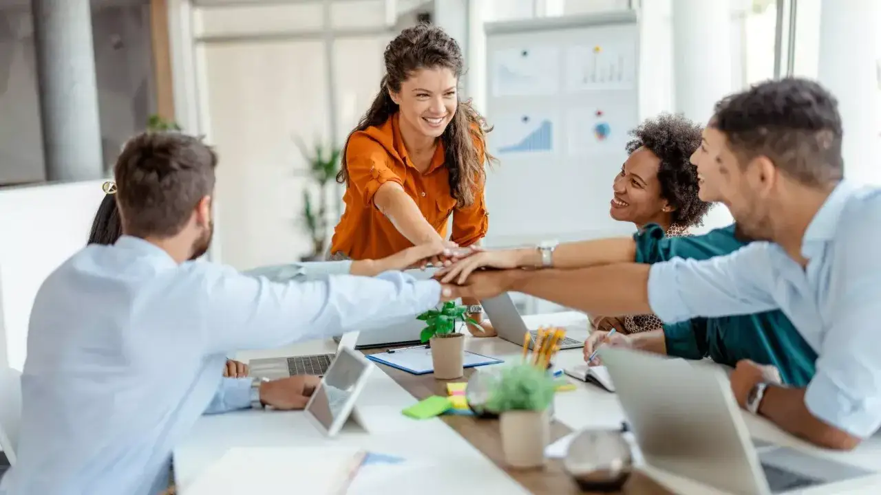 A diverse team in an office, hands stacked in a gesture of unity, showing that can trust be rebuilt through collaboration and shared success.