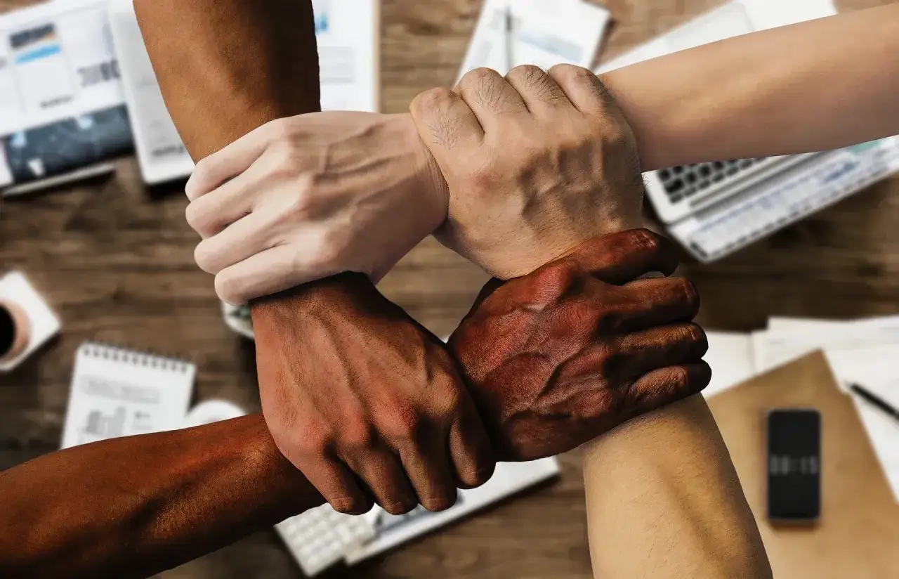 Four hands of different skin tones interlock, symbolizing psychological trust and unity in a collaborative environment.
