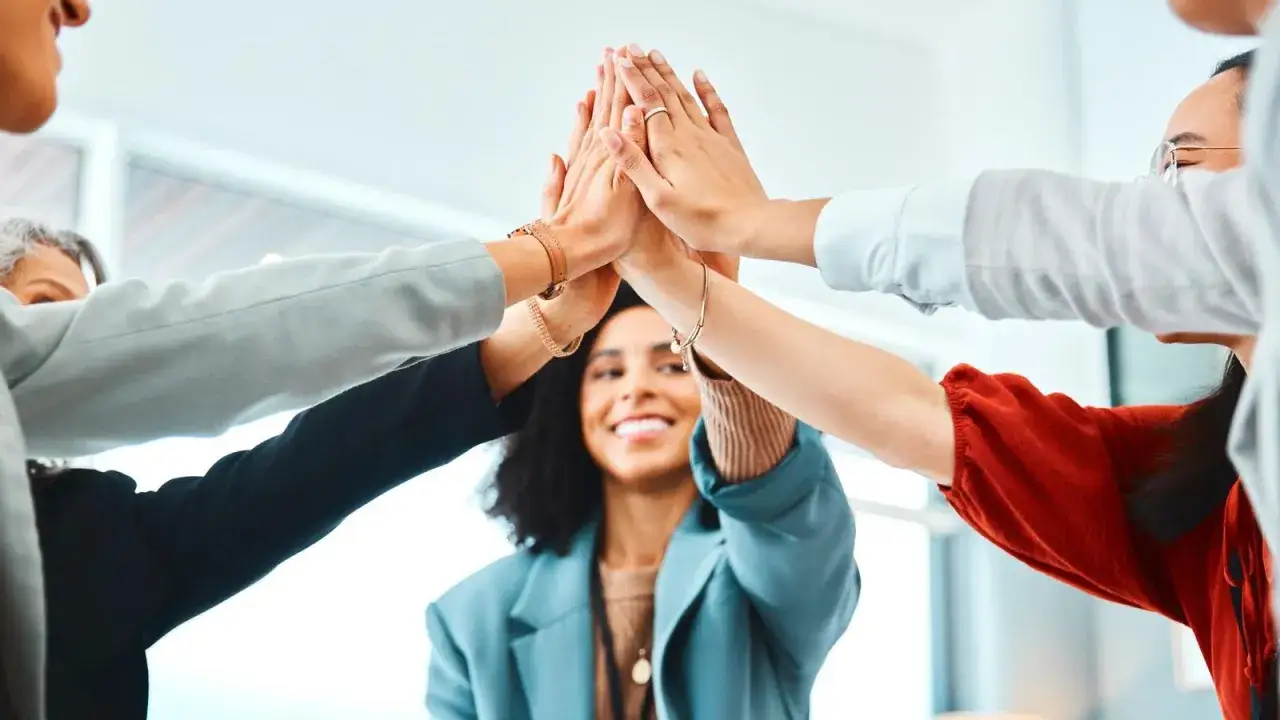 A diverse team high-fiving, celebrating success and positive stages of employee experience.