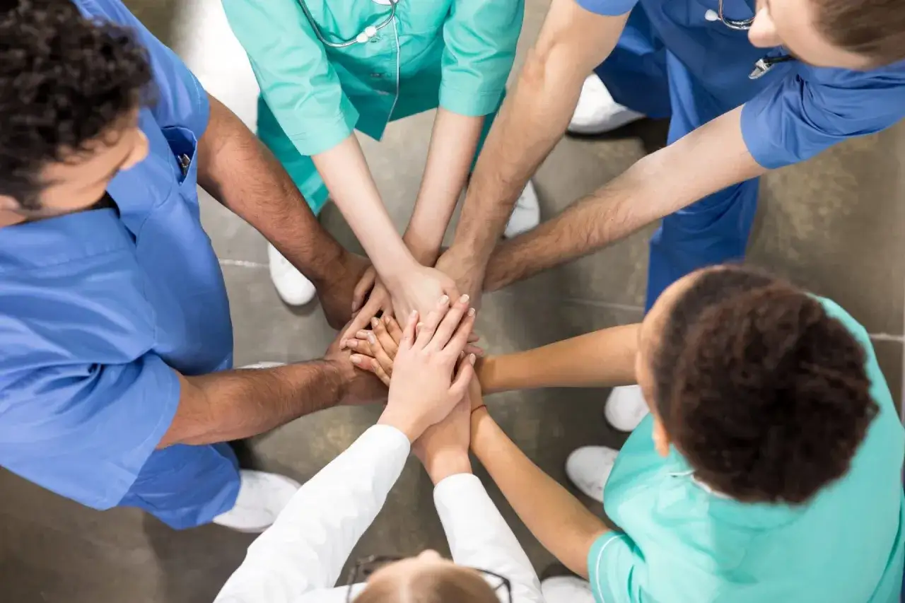 A diverse team of medical professionals demonstrates adaptability in leadership by uniting their hands, symbolizing collaboration and shared commitment to patient care.