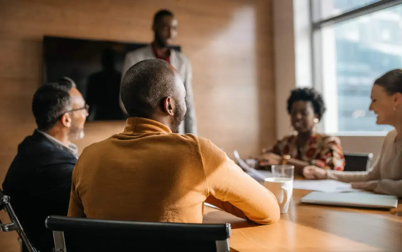 Diverse team in a meeting room, engaged in manager training. A presenter stands while others listen attentively.