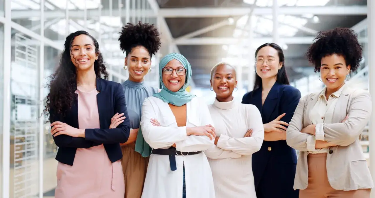Diverse women in business attire, smiling confidently. This image represents successful leadership development for women, showcasing a team ready to conquer challenges.