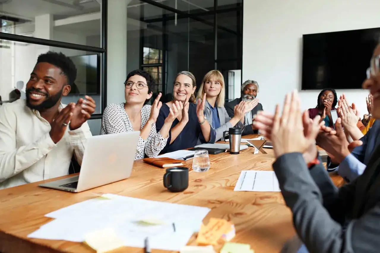 A diverse group of people in a meeting room are clapping, celebrating a successful communication podcast.