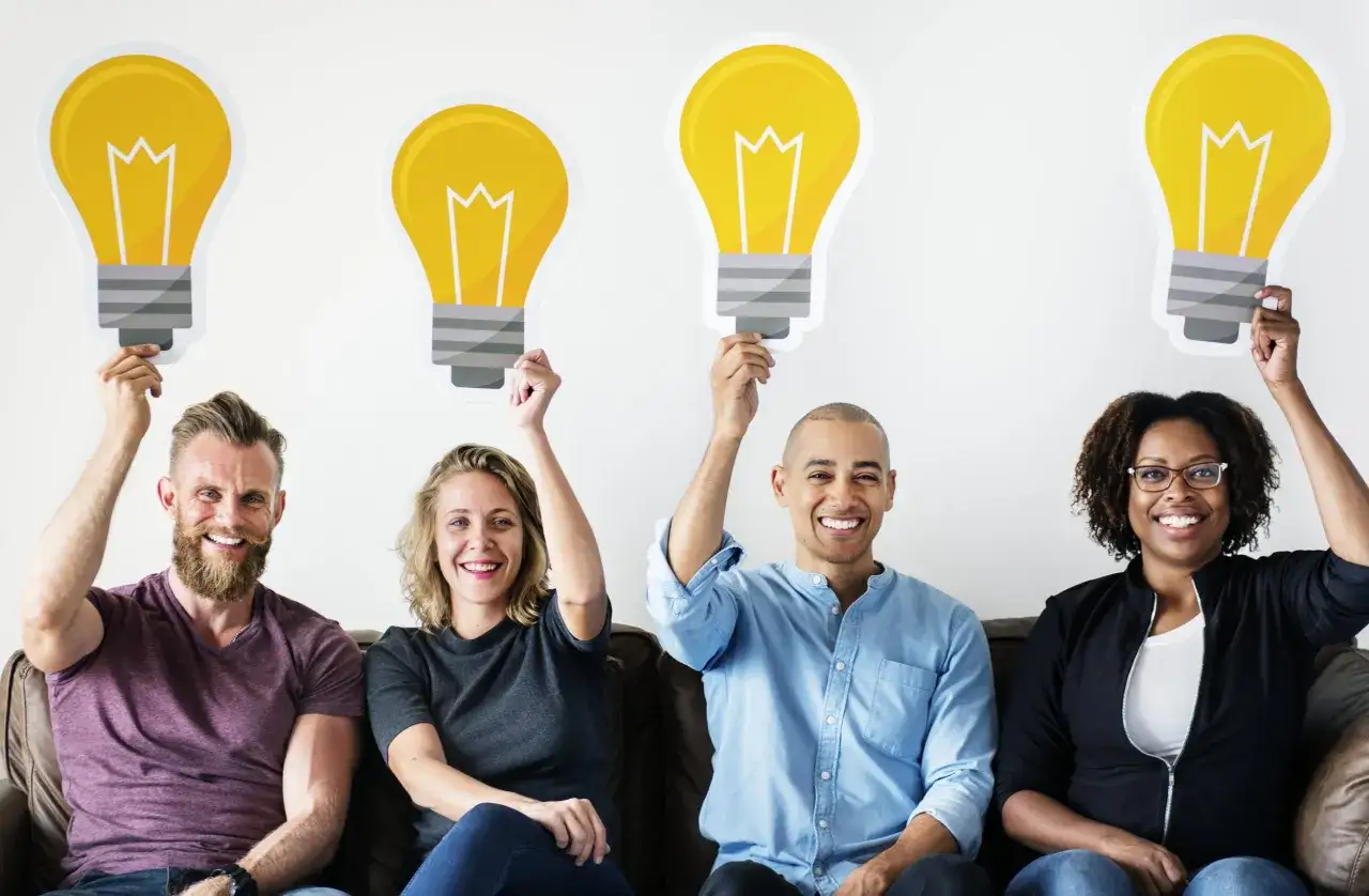 Four smiling people hold up lightbulb cutouts, symbolizing a workplace where psychological safety fosters innovation and bright ideas.