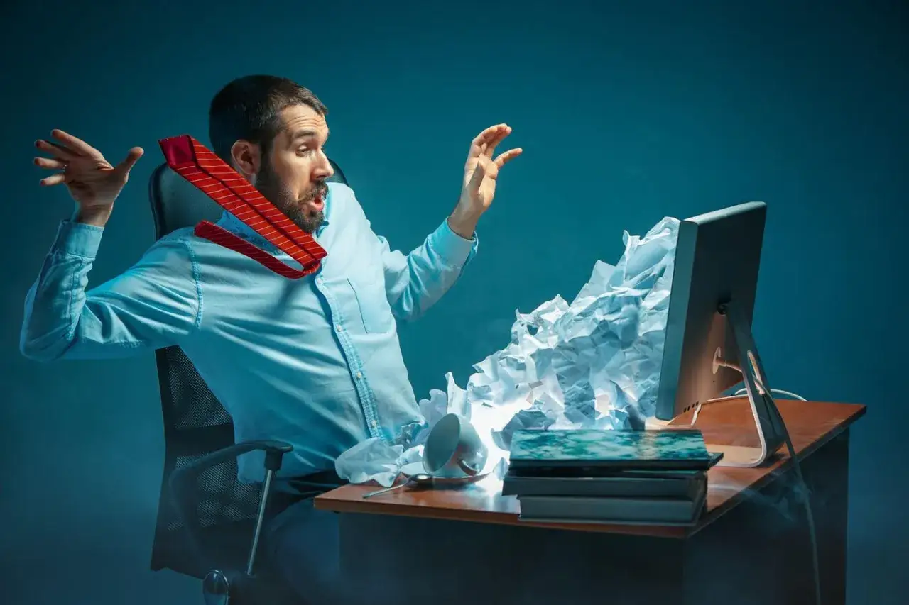 A man in a blue shirt, tie askew, throws his hands up in exasperation as crumpled paper erupts from his computer screen, a visual metaphor for trying to break through the noise.